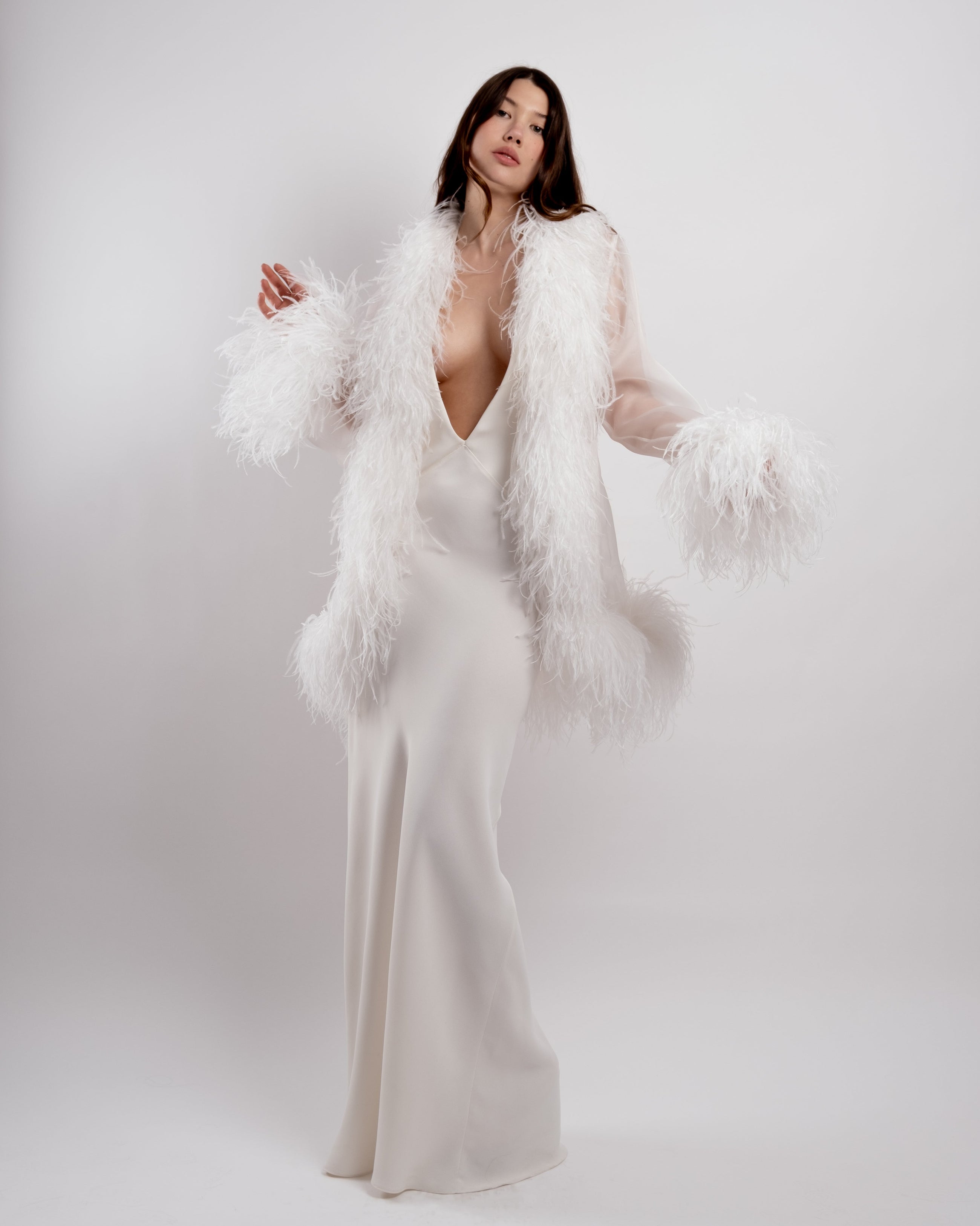 Woman wearing a white dress with a feathered cover-up against a white background