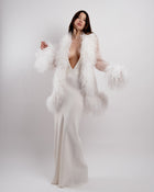 Woman wearing a white dress with a feathered cover-up against a white background